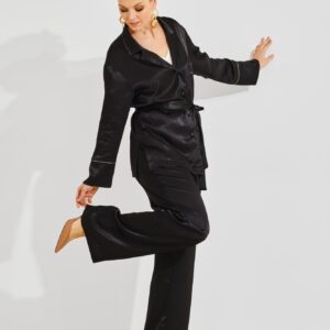 Woman in black loungewear touching the heel of her shoe against a minimalist white backdrop