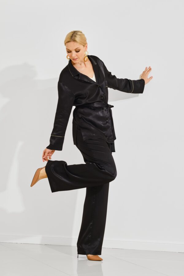 Woman in black loungewear touching the heel of her shoe against a minimalist white backdrop